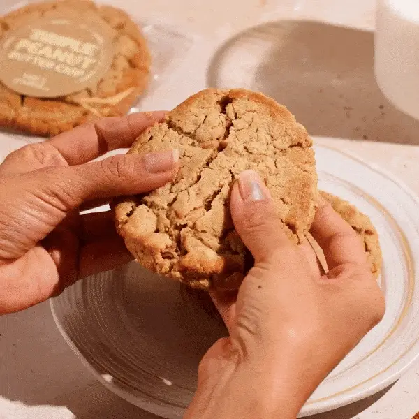 peanut butter cookie being broken apart and dipped in milk