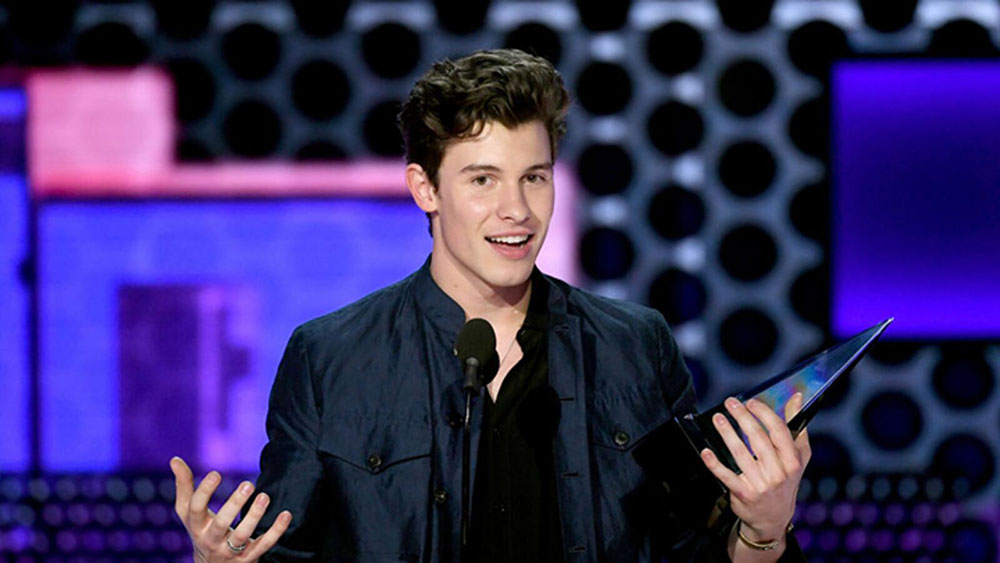 Photo of Shawn Mendes holding award in blue jacket