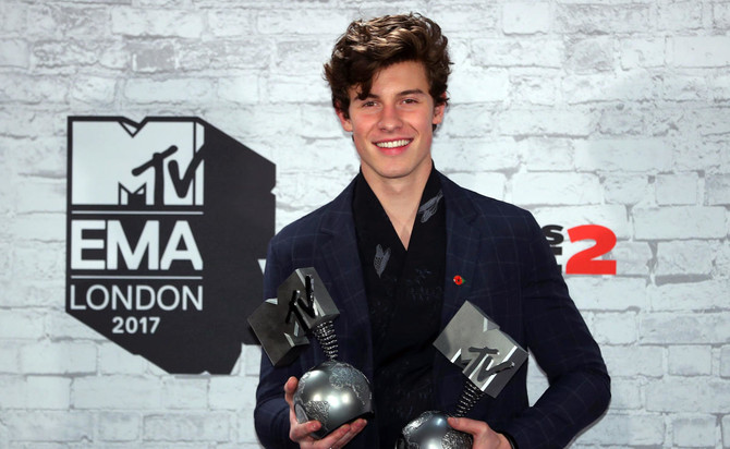 Photo of Shawn Mendes holding two MTV awards and in a blue suit