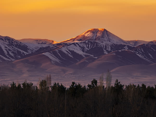 Large snowy mountain in front of smoky orange sunset