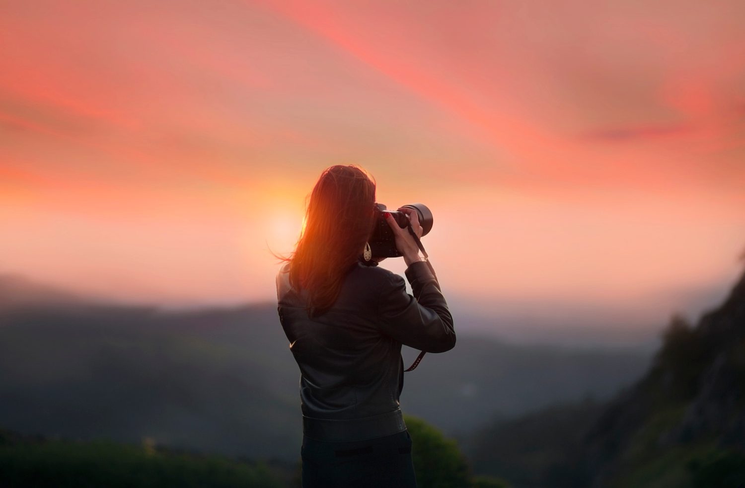 Woman taking a photo of a sunset on a cliff