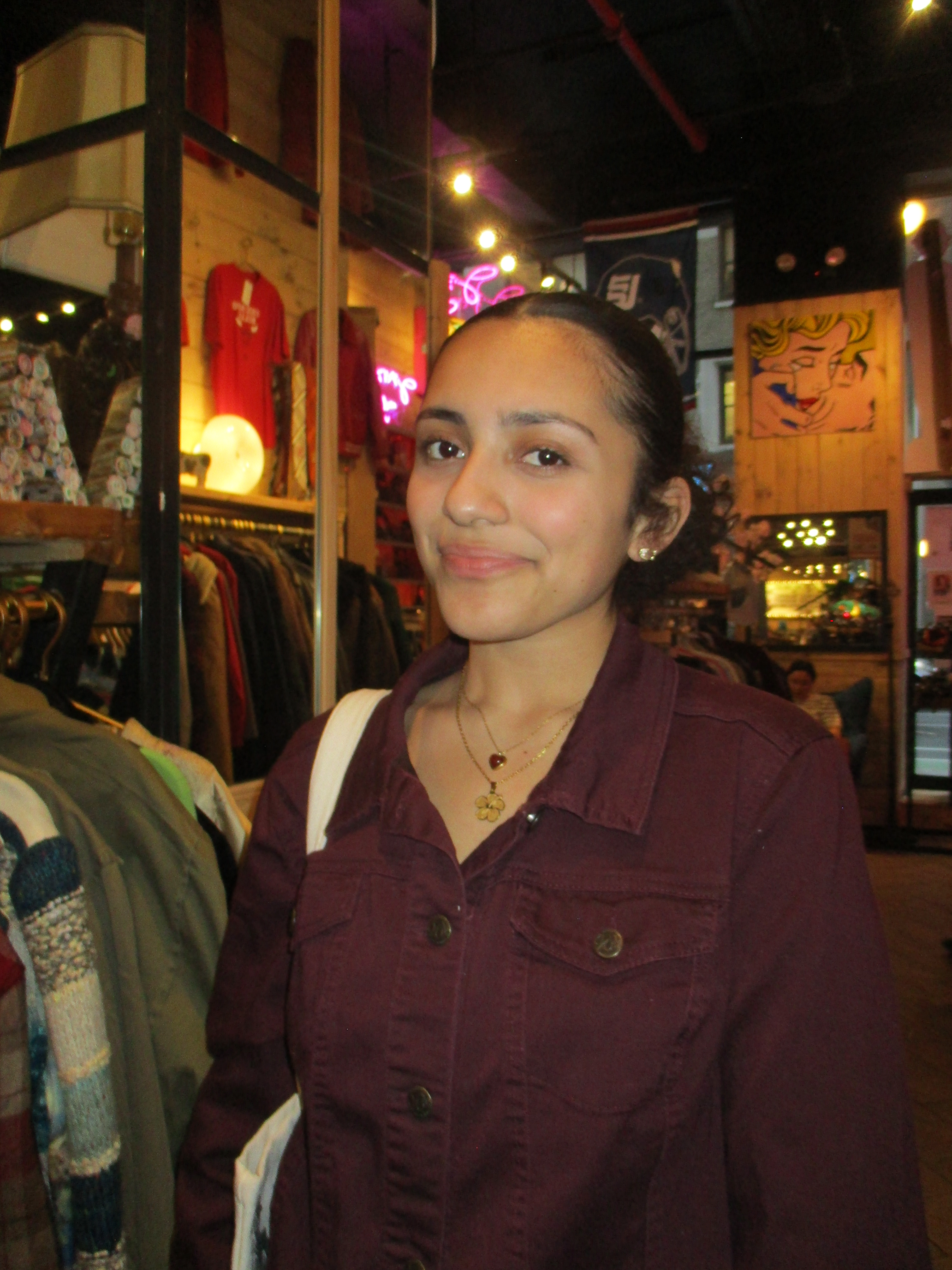 Picture of girl with slicked black hair, wearing a golden necklace and holding a bag