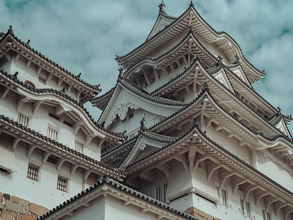 A traditional japanese castle with slopped, shingled roofs and stucco walls.